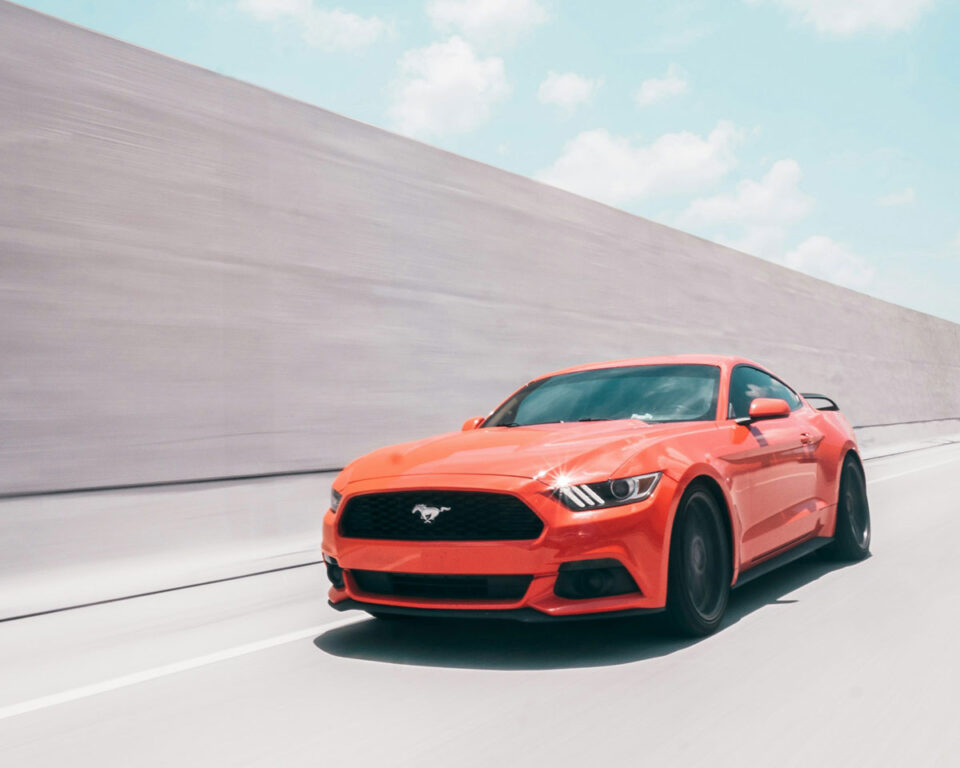 orange ford mustang driving on the road
